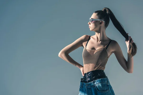 Niña posando en gafas de sol con peinado de cola de caballo, aislado en gris - foto de stock