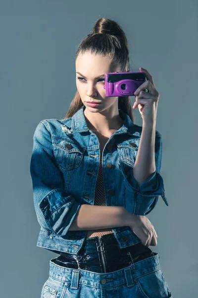 Menina morena posando em roupas jeans com câmera retro, isolado em cinza — Fotografia de Stock