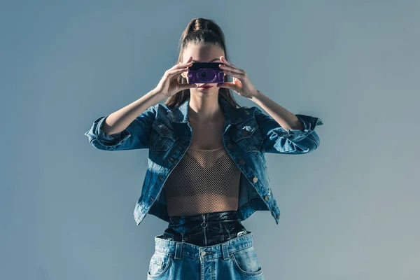 Modisches Mädchen posiert in Jeanskleidung mit Retro-Kamera, isoliert auf grau — Stockfoto