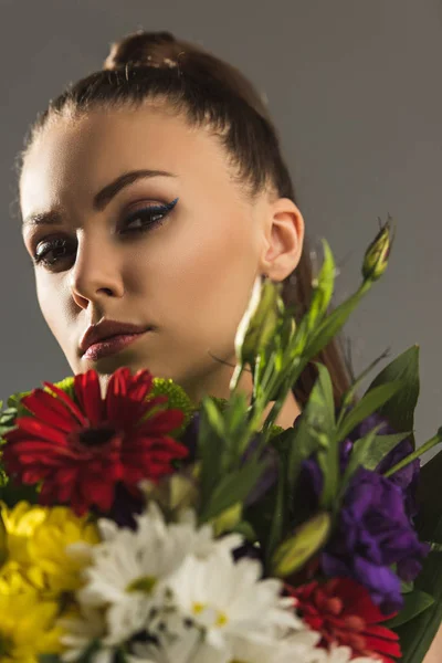 Portrait of beautiful girl with bouquet of flowers looking at camera, isolated on grey — Stock Photo