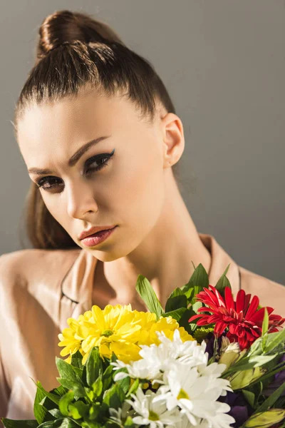 Retrato de mujer joven atractiva con ramo de flores, aislado en gris - foto de stock