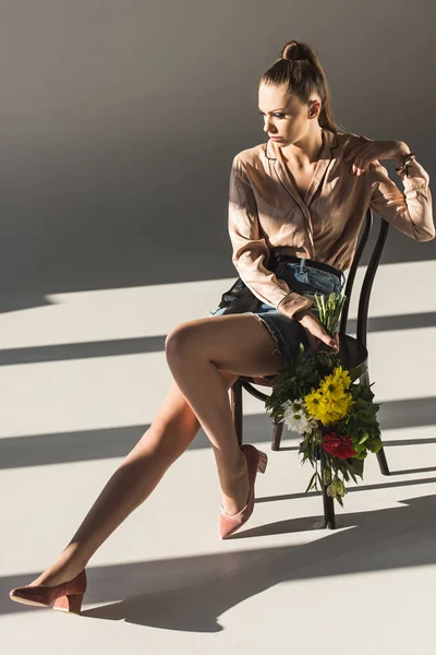 Schöne modische Mädchen mit Blumenstrauß posiert auf Stuhl — Stockfoto