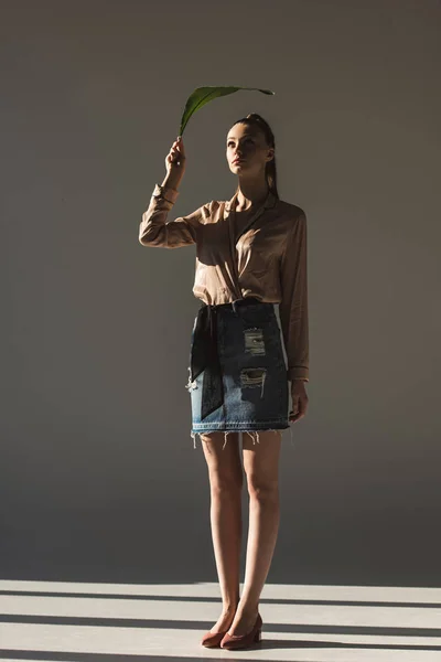 Fashionable model in denim skirt and blouse holding green leaf — Stock Photo