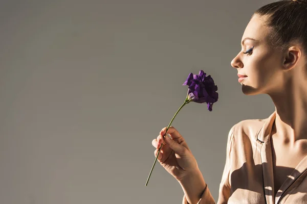 Красива жінка дивиться на фіолетову квітку еустоми, ізольована на сірому — стокове фото