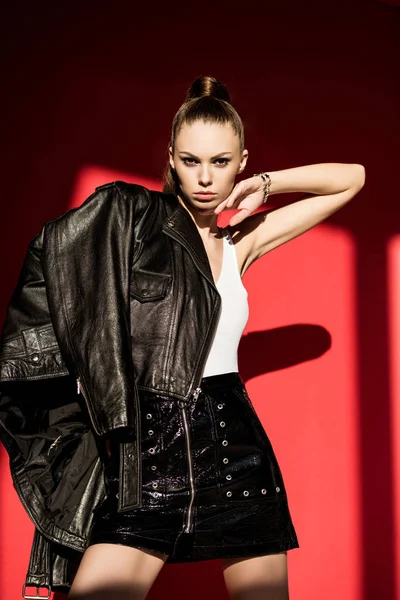 Stylish caucasian girl posing in black leather jacket for fashion shoot on red — Stock Photo