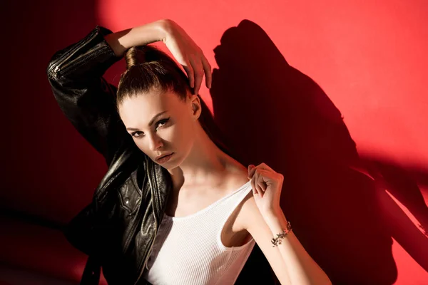 Beautiful girl posing in black leather jacket for fashion shoot on red — Stock Photo