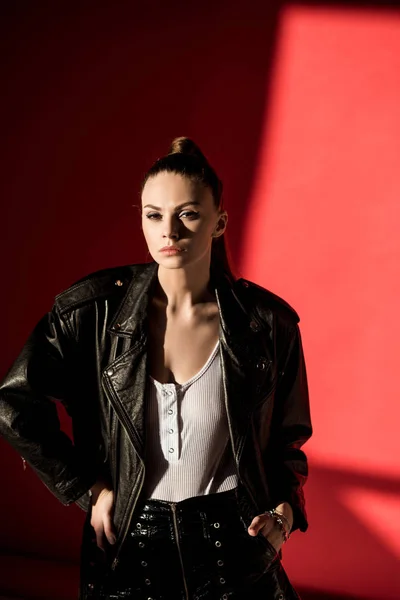 Attractive young woman posing in black leather jacket for fashion shoot on red — Stock Photo