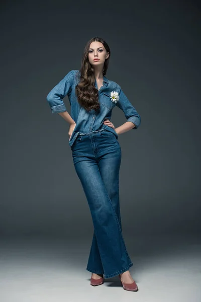 Beautiful girl with long hair posing in flare jeans, on grey — Stock Photo