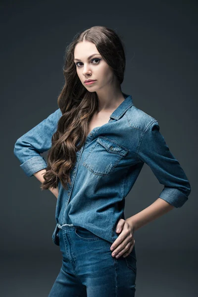 Bonita chica con el pelo largo morena posando en ropa de mezclilla, aislado en gris - foto de stock