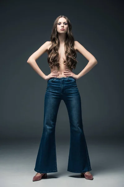 Beautiful half naked girl with long hair posing in flare jeans, on grey — Stock Photo