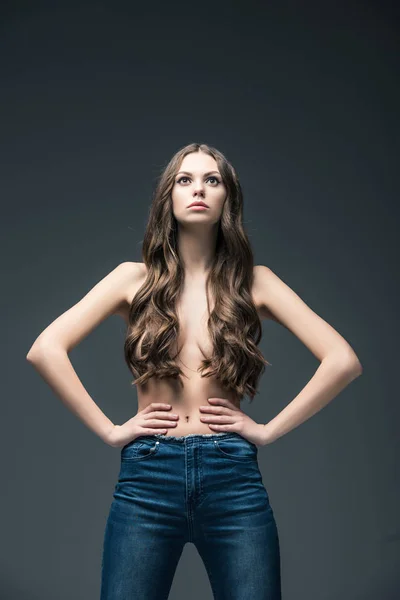 Atractiva chica semidesnuda con el pelo largo posando en jeans, aislado en gris - foto de stock