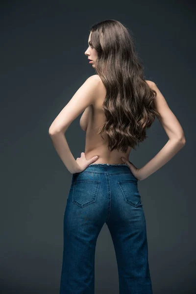 Вид на полуобнаженную женщину с длинными волосами, позирующую в джинсах, изолированную на сером — стоковое фото