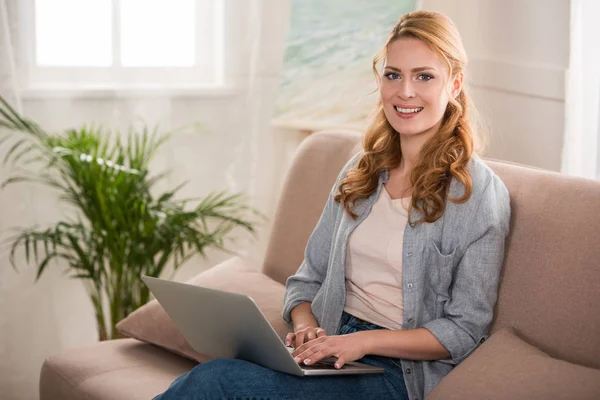 Belle jeune femme en utilisant un ordinateur portable et souriant à la caméra — Photo de stock