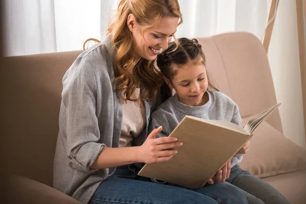 Feliz madre e hija pequeña leyendo el libro juntos en casa - foto de stock