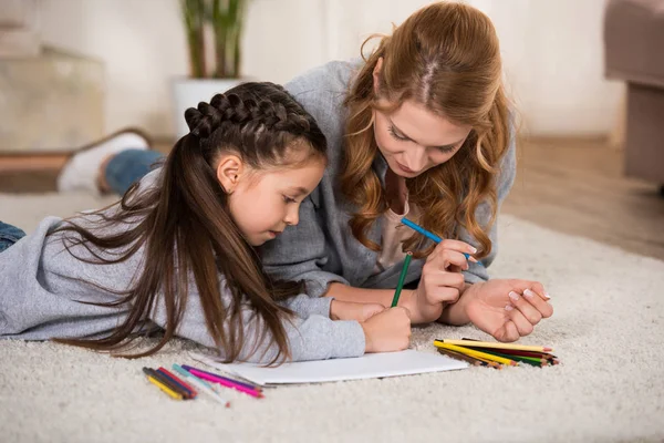 Madre e hija dibujando con lápices de colores en casa - foto de stock