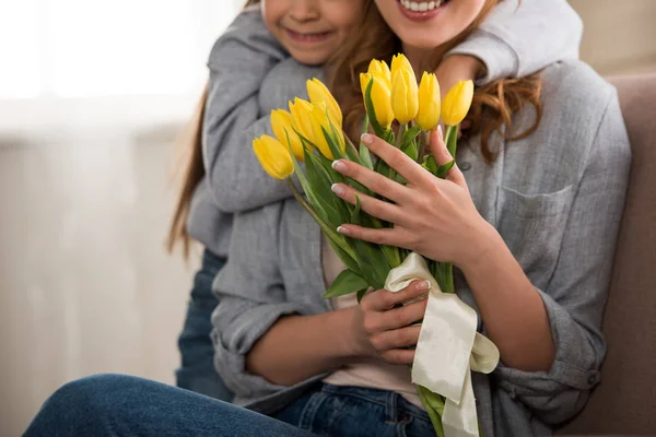 Plan recadré d'enfant heureux étreignant mère souriante avec des tulipes jaunes — Photo de stock