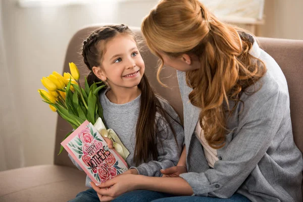 Beautiful smiling mother and daughter holding yellow tulips and happy mothers day greeting card — Stock Photo