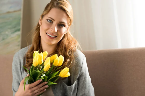 Attraktive junge Frau mit gelben Tulpen, die in die Kamera lächelt — Stockfoto