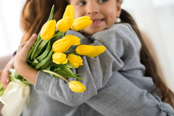 Recortado disparo de adorable niño sosteniendo tulipanes amarillos y abrazando a la madre - foto de stock