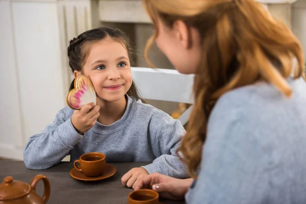 Selective focus of happy child holding heart shaped cookie and looking at mother — Stock Photo