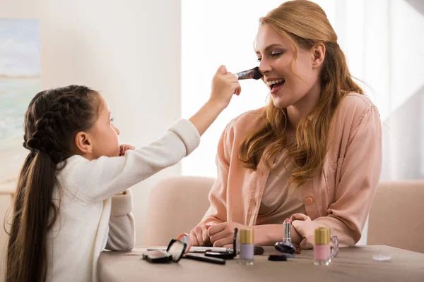 Mãe feliz e filhinha aplicando maquiagem juntos em casa — Fotografia de Stock