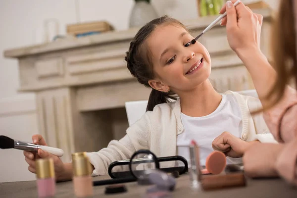 Plan recadré de la mère appliquant le maquillage à adorable petite fille heureuse — Photo de stock