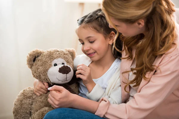 Beautiful happy mother and daughter playing with teddy bear at home — Stock Photo