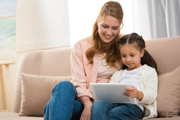 Hermosa sonriente madre e hija usando tableta digital juntos en casa - foto de stock