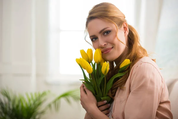 Glückliche junge Frau hält gelbe Tulpen in der Hand und lächelt in die Kamera — Stockfoto