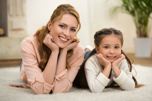 Hermosa madre feliz y la hija acostada en la alfombra y sonriendo a la cámara - foto de stock