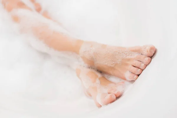 Vista parcial de las piernas femeninas en baño con espuma - foto de stock