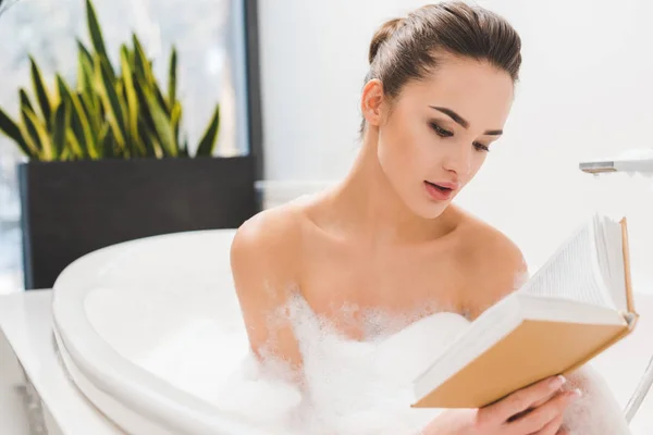 Portrait of young woman reading book while taking bath — Stock Photo