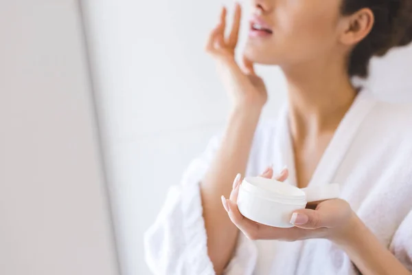 Cropped shot of beautiful woman in bathrobe applying face cream — Stock Photo