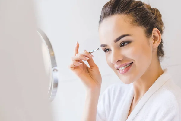 Young woman plucking eyebrows with tweezers — Stock Photo