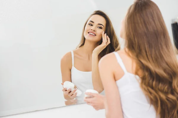 Miroir reflet de belle femme appliquant crème visage — Photo de stock