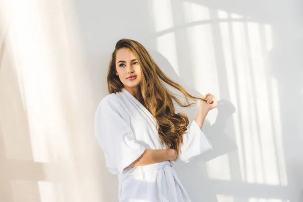 Portrait of pretty young woman in bathrobe leaning on white wall at home — Stock Photo