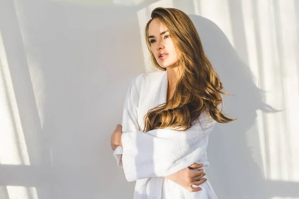 Porträt einer hübschen jungen Frau im Bademantel, die zu Hause an eine weiße Wand lehnt — Stockfoto