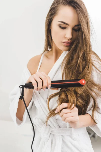 Retrato de mujer alisando el cabello con alisador de pelo - foto de stock