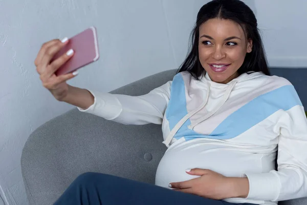 Улыбающаяся африканская беременная женщина делает селфи на смартфоне — стоковое фото