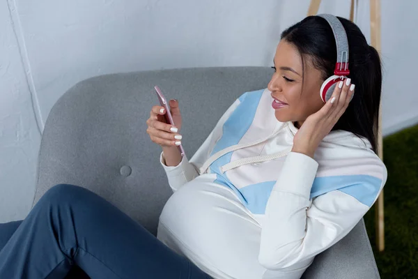 Mulher grávida afro-americana ouvindo música com fones de ouvido e usando smartphone — Fotografia de Stock