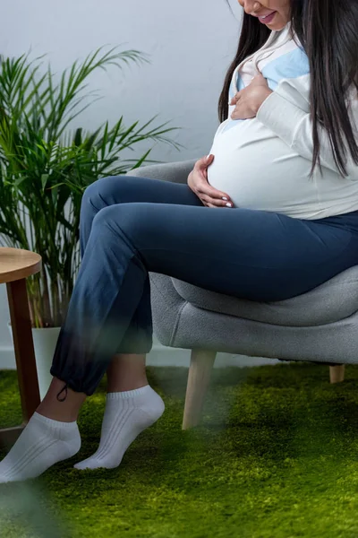 Обрізаний вид вагітної жінки, що сидить у кріслі вдома — стокове фото