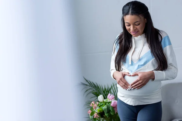 Afro-américaine enceinte femme faisant symbole de coeur avec les mains sur le ventre — Photo de stock