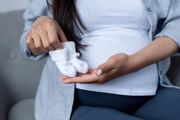 Vista cortada de mulher grávida segurando pequenas meias — Fotografia de Stock