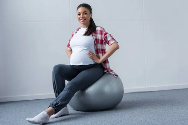 Щаслива афро-американська вагітна жінка сидить на підходящому м'ячі — стокове фото