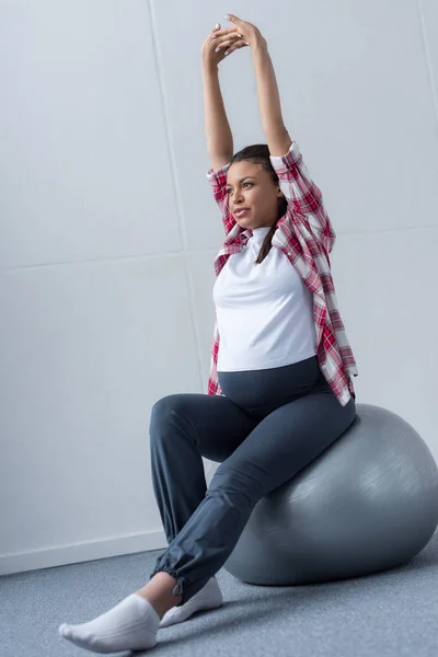 Deportivo africano americano embarazada mujer estiramiento en ajuste bola - foto de stock