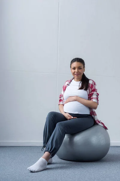 Lächelnde afrikanisch-amerikanische schwangere Frau sitzt auf fittem Ball — Stockfoto