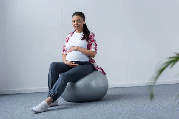 Deportivo africano americano embarazada mujer sentado en fit bola - foto de stock