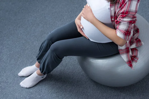 Vista recortada de la mujer embarazada sentada en la bola en forma - foto de stock