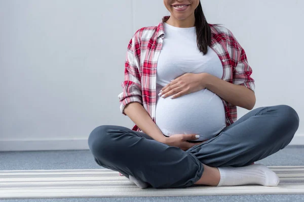 Vista ritagliata di donna africana americana incinta seduta su tappetino yoga — Foto stock