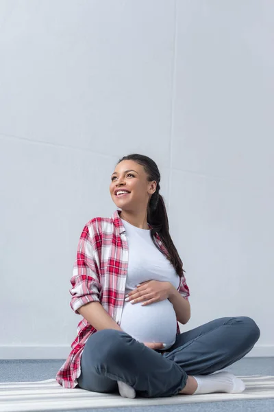 Glücklich afrikanisch-amerikanische schwangere Frau sitzt auf Yogamatte — Stockfoto